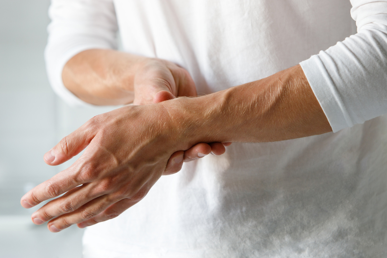 Man Wearing White Sweater Holding His Left Wrist with Force